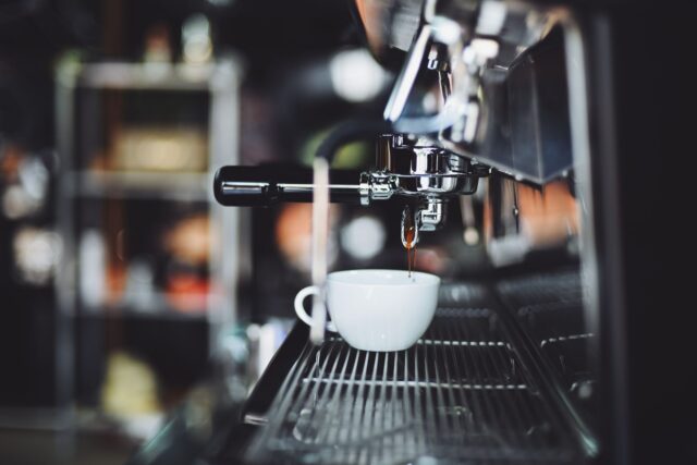 Espressor profesional pe tejgheaua unei cafenele mici, cu cești pregătite pentru servire